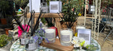 Table with candles, diffusers, and decorative items on a patio with a stone building in the background.